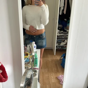 Vit ribbad croppad tröja - Säljer en vit croppad tröja med ribbat mönster och långa ärmar. Tröjan har en snygg, figurnära passform och hög halsringning. Perfekt att styla med jeans eller kjol för en clean look.