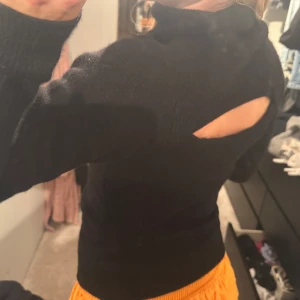 Svart polotröja med öppen rygg - Svart polotröja i stickat material med lång ärm och en snygg cut out-detalj på ryggen. Tröjan har en hög krage och sitter tajt mot kroppen, perfekt för dig som vill ha en stilren men ändå unik look. I ullmaterial