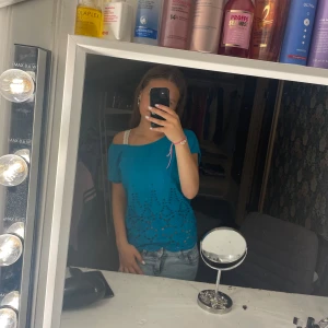 Turkos blus - Snygg turkos blus med korta ärmar och broderade hålmönster nertill. Blusen har en lös passform och rund halsringning, perfekt för en chill och somrig vibe. Materialet känns lätt och luftigt, vilket gör den skön att bära varma dagar.