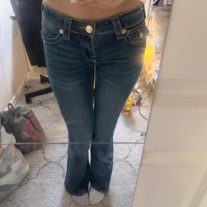 True Religion Joey Low Rise Flare jeans - Säljer ett par blå True Religion Joey Low Rise Flare jeans i storlek 25. De har låg midja, utsvängda ben och snygga ficklock med gul kontrastsöm och stora knappar. Klassisk denim med coola detaljer och ikonisk bakficka. Helt nya inte använda 🩷 priset kan diskuteras 