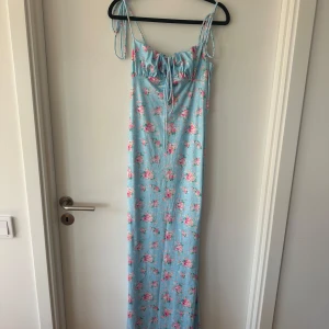 Blommig långklänning med snörning - Supersöt ljusblå långklänning med rosa blommor och smala axelband som knyts. Klänningen är från SHEIN och helt oanvänd!