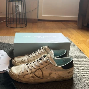 Philippe Model vita sneakers  - Snygga vita sneakers från Philippe Model med svart detalj på hälen och klassisk snörning. Skorna har en rund tå och är tillverkade i skinn med en platt sula. Perfekta för dig som gillar en urban och avslappnad stil. Helt okej skick, använda ganska mycket. Men är fortfarande användbara. Dustbag, box mm följer med. Lägg gärna ett prisförslag och få skorna billigare vid snabbaffär. 