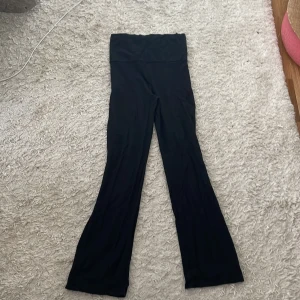 Svarta vida yogabyxor med en vikbar överdel  - Säljer ett par svarta yogabyxor med vikbar överdel midja och utsvängda ben. Byxorna är i ett mjukt och stretchigt material som sitter skönt på kroppen. Perfekta för dig som gillar en loose och bekväm stil med lite extra längd i benen.