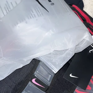 Nike elite ryggsäck  - Säljer en svart Nike ryggsäck med coola detaljer i rosa och blått på axelremmarna. Väskan har tydlig Nike-logga och genomskinliga plastpaneler som ger en sportig vibe. Perfekt för dig som vill sticka ut med en snygg och funktionell väska.säljer den på grund av att den har aldrig kommit till användning 