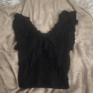 Svart volang topp från Zara - Supersöt svart topp från Zara med volangdetaljer och v-ringning. Stickad känsla med spetsinslag och ärmlös design. Perfekt för dig som gillar romantiska och trendiga plagg med extra detaljer. Super fin topp till sommaren💞💞