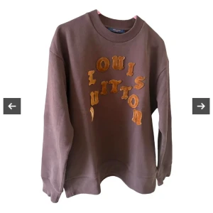Brun Louis Vuitton sweatshirt - Säljer en brun sweatshirt från Louis Vuitton med stora, gula bokstäver i plysch på bröstet. Tröjan har rund hals, långa ärmar och en relaxed passform. Perfekt för dig som vill sticka ut med ett lyxigt streetwear-plagg.