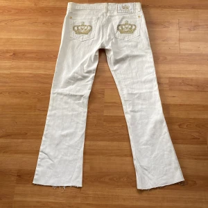 Vita bootcut jeans från Victoria beckham - Rock & Republic - Snygga vita lågmidjade bootcut jeans från Rock & Republic med guldiga broderade kronor på bakfickorna och avklippta benslut. Jeansen har guldiga detaljer och klassisk femficksdesign. MÅTT: Innerbenslängd 69cm, midjemått (tvärsöver) 37cm.  Står att det är strlk 27 men skulle säga 25 eller 26.   ‼️PRIS KAN DISKUTERAS‼️❤️Bra skick! 