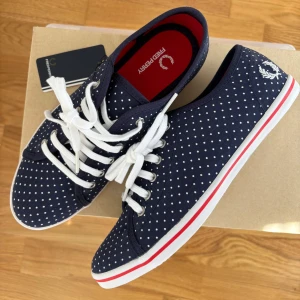 Mörkblå prickiga sneakers/tygskor Fred Perry - Nätta, söta mörkblå sneakers/tygskor från Fred Perry med vita prickar. Köpta för några år sen men oanvända med lappar kvar. Storlek 37 men smal modell så funkar nog om du är mellan 36-37 också.  Perfekta för dig som gillar en sportig och stilren preppy look 💞Säljer för att de är lite för små