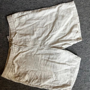 Beiga linneshorts från H&M Regular Fit - Snygga beiga shorts från H&M i regular fit med dragsko i midjan. Tillverkade i svalt linne, perfekta för varma dagar. Klassisk design med fickor på sidorna och baktill. Lätta att matcha med t-shirt eller skjorta för en chill look.