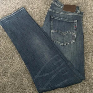 Blå jeans Replay Rocco straight fit - Säljer ett par blå jeans från Replay, modell Rocco. Jeansen har klassisk femficksdesign, raka ben och snygga slitningar på benen. De är tillverkade i jeansmaterial och har en mörkblå tvätt med ljusare partier. Hör av er vid frågor eller funderingar