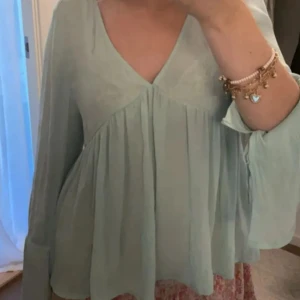 Ljusgrön blus med spets och v-ringning - Supersöt ljusgrön blus med v-ringning och långa, vida ärmar. Baksidan har transparent spets och en liten knytning i nacken. Blusen är luftig och har ett flowy fall, perfekt för dig som gillar romantiska detaljer. Står storlek 42 men skulle säga mer 36/38