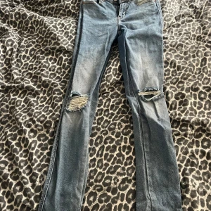 Blå ripped jeans från Dr Denim - Säljer ett par blå jeans från Dr Denim, modell Lexy Westcoast Blue Ripped. De har snygga slitningar över knäna och en smal passform. Jeansen är i klassisk denim med stretch och har en modern look.