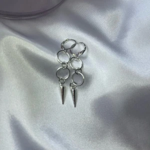 Silvriga örhängen med ringar och spikes - Säljer ett par coola silvriga örhängen med tre sammanlänkade ringar och en spetsig spike längst ner. De har en modern och edgy vibe, perfekta för att lyfta din stil. Passar dig som gillar statement-smycken och vill sticka ut lite extra.