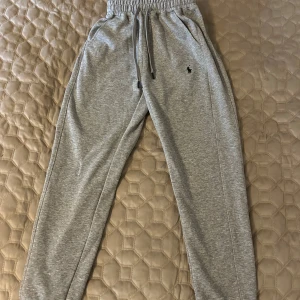 Grå mjukisbyxor Polo Ralph Lauren - Grå mjukisbyxor från Polo Ralph Lauren med broderad svart logga på höften. Byxorna har dragsko i midjan och är i en slim passform. Perfekta för chill dagar eller när du vill vara bekväm men ändå se snygg ut.