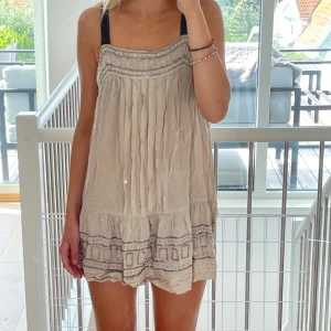 Beige kortklänning från Next - Supersöt beige kortklänning från Next med volangkant och dekorativa paljettdetaljer upptill och nertill! 