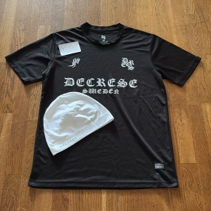 Svart t-shirt från Decrese Sweden - Svart t-shirt från Decrese Sweden med vit gotisk text på bröstet och liten patch nertill. Klassisk rund hals och korta ärmar. Tillverkad i Sverige, känns sportig och lätt med polyesterkänsla. Perfekt för dig som gillar streetwear med edge.  01