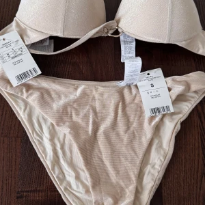 Glittrig bikini Golden Gleam Coco - Supersnygg glittrig bikini set i ljus champagnefärg från calzedonia . Överdelen har vadderade pushup kupor och en snygg ringdetalj framtill. Materialet är glansigt och känns lyxigt mot huden. Perfekt för strandhäng och poolparty!