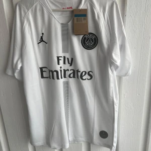 PSG Neymar Jr vit matchtröja Jordan - Snygg vit PSG fotbollströja med Neymar Jr och nummer 10 på ryggen. Jordan-logga på bröstet, Fly Emirates-tryck och PSG-märke framtill. Kortärmad modell i lätt och ventilerande material, perfekt för match eller träning.