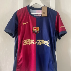 FC Barcelona x Nike fotbollströja S - Snygg FC Barcelona fotbollströja från Nike i storlek S. Tröjan har klassisk halva-röd halva-blå design med guldiga detaljer och tryck, klubbmärke på bröstet och sponsorloggor. Tillverkad i lätt och ventilerande polyester, perfekt för match eller träning.