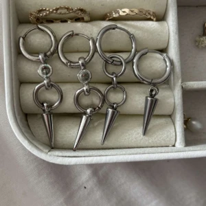 Silvriga örhängen med spikes - Coola silvriga örhängen med hoops och hängande konformade spikes. Några har extra ringar och små detaljer som ger en edgy vibe. Perfekta för dig som gillar statement-smycken med attityd. De två längre rostar och de två kortare är rostfritt stål!