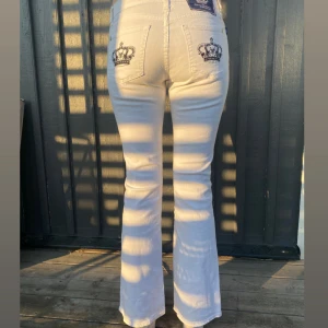 Vita jeans från Victoria Beckham - Snygga vita jeans från Victoria Beckham. Dom är bootcut och har unika broderade kronor på bakfickorna. Perfekta för dig som vill sticka ut med stilrena detaljer. Säljer dom för att dom är för stora mig. Tjejen på bilden är 182 cm lång.