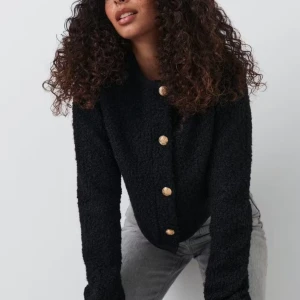 Svart teddykofta med guldknappar - Svart teddykofta med lång ärm och snygga guldknappar framtill. Jackan har en rund halsringning och är gjord i ett mjukt, fluffigt material som ger en cool och trendig look. Perfekt för dig som vill ha en mysig men stilren kofta.