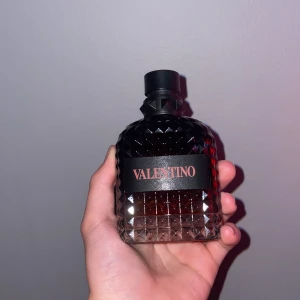Valentino parfym 100ml - Säljer en lyxig parfym från Valentino, 100ml Eau de Parfum. Flaskan är i mörktonat glas med coolt nitat mönster och svart kork. Märket står tydligt på framsidan. Perfekt för dig som gillar exklusiva dofter och snygg design.