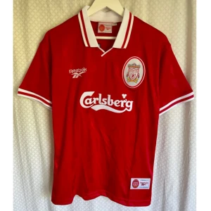 Vintage Jersey Liverpool FC   - Klassisk röd Liverpool FC match hemmatröjan säsong 1996/1997 från Reebok med Carlsberg-tryck, klubbmärke på bröstet och vit krage. Nummer 7 och McManaman på ryggen. Kortärmad modell i lätt och glansigt material, perfekt för fotbollsfans.