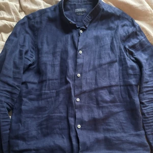 Mörkblå linneskjorta från Zara Man - Snygg mörkblå skjorta från Zara Man i slim fit-modell. Tillverkad i svalt linne med klassisk krage och vita knappar framtill. Perfekt för dig som gillar stilrena och enkla plagg med modern passform.