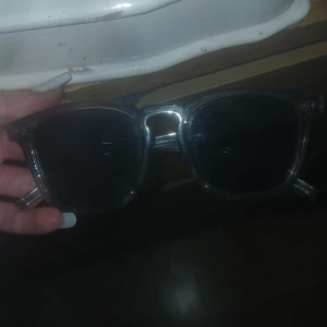 Transparenta solglasögon med svarta glas - Snygga solglasögon med transparent båge och svarta glas. Klassisk fyrkantig form som passar till de flesta stilar. Bågarna är i plast och ger en modern vibe. Perfekta för soliga dagar när du vill se cool ut.