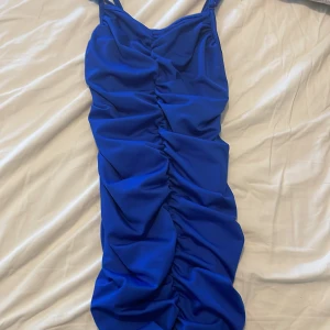 Blå ruched kortklänning från SHEIN - Supersnygg blå kortklänning från SHEIN med smala axelband och ruched detalj framtill. Klänningen har en tight passform och är perfekt för dig som vill sticka ut. Gjord i ett mjukt och stretchigt syntetmaterial som sitter bekvämt hela dagen.