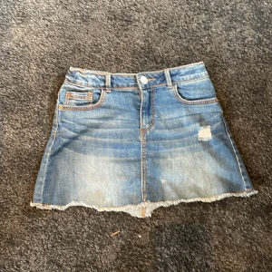 Blå jeanskjol från Zara Kids - Snygg blå jeanskjol från Zara Kids med slitna detaljer och rå kant nertill. Klassisk femficksmodell med knapp och dragkedja framtill. Perfekt för sommaren!🌸💕