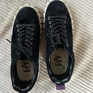Svarta Eytys odessa  - Snygga svarta sneakers från Eytys i mocka med kraftig vit sula och lila hälflik. Skorna har rund tå, svarta skosnören och metallöljetter. Perfekta för dig som gillar chunky streetstyle och vill sticka ut med detaljer.