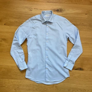 J.Lindeberg Skjorta - Snygg ljusblå skjorta från J.Lindeberg i slim fit-modell. Tillverkad i mjuk bomull som känns skön mot huden. Perfekt för dig som gillar stilrena och fräscha plagg. Den kan upplevas en aning glansig på bilderna men den är inte det i verkligheten. Den är använd 1 gång. Nypris ligger runt 1400kr. Storleken är som en Medium