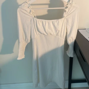 Vit kortklänning med snörning - Supersöt vit kortklänning med puffärmar och smockade ärmslut.