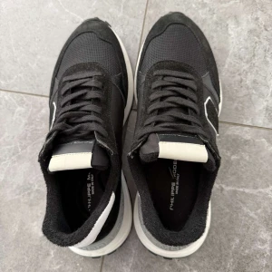 Svarta sneakers från Philippe Model - Snygga svarta sneakers från Philippe Model med vit och grå detalj på hälen och vit sula. Ovandelen är i en mix av mocka och textil, med snörning och en cool logga på sidan. Perfekta för dig som gillar stilrena och sportiga skor. Dm för frågor🙌