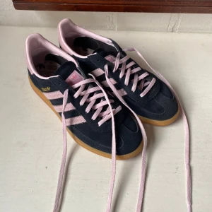 Adidas Spezial sneakers svart/rosa - Snygga Adidas Spezial sneakers i svart mocka med ljusrosa detaljer och klassiska tre ränder. Skorna har rosa snörning, gummisula och guldfärgad logga på sidan. Perfekta för dig som vill ha en retro vibe med modern touch. De är använda ett väldigt väldigt lågt antal gånger och är alltså nästintill nya, köptes i New York i april. Skon passar ungefär storlek 38/39. 
