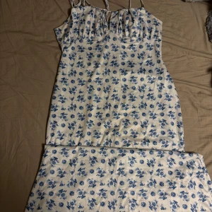 Vit långklänning med blå blommor - Supersöt långklänning i vitt med blått blommönster och smala axelband som knyts. Klänningen har en romantisk vibe med rynkade detaljer vid bysten och är perfekt för varma dagar. Materialet känns lätt och flowy. StorlekXl passar L och M 