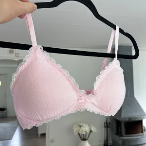 Söt ljusrosa bh med spets (NY) - Ljusrosa bh med smala axelband och fina spetsdetaljer längs kanterna. Den har diskret ribbat mönster och en liten rosett framtill. Perfekt för en gullig och feminin look. Inköpt på Kmart i Australien. Aldrig använd!!! (köpte fel storlek) 🩷