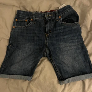 Levi's 511 jeansshorts blå denim - Snygga blå jeansshorts från Levi's modell 511 med klassisk femficksdesign, uppvikta benslut och tydliga kontrastsömmar. Shortsen har Levi's-logga på insidan av linningen och läderpatch bak. Perfekta för en chill sommarstil.