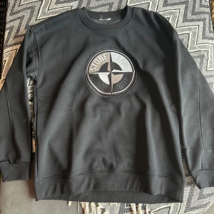 Stone Island sweatshirt med stor logga - Två feta sweatshirts från Stone Island med stor broderad logga på bröstet. En i svart och en i grått, båda med rund hals och ribbade muddar. Perfekt för dig som vill ha en clean och stilren look med streetkänsla.