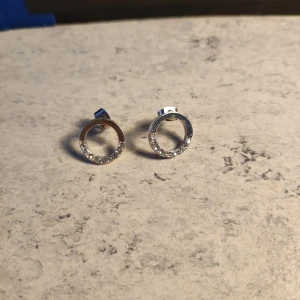 Glittriga cirkelörhängen i silver - Snygga örhängen i form av öppna cirklar i silverfärg med glittrande stenar längs kanten. Perfekta för dig som gillar stilrena smycken med lite extra bling. Små och smidiga att bära varje dag.