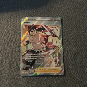 Bruno (Trainer, Single Strike) - Cool och glittrig Pokémonkort med Bruno, en kraftfull tränare från Single Strike-serien! Perfekt för dig som samlar eller vill boosta din lek med en supporter som ger dig extra kort. Snyggt motiv och populär bland unga Pokémonfans. Den är riktigt cool