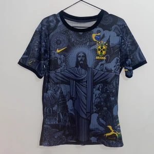 Brasil Nike fotbollströja mörkblå - Snygg mörkblå Brasilien fotbollströja från Nike med unikt grafiskt tryck av Kristusstatyn och brasilianska motiv. Tröjan har korta ärmar, rund hals och Brasil CBF-emblem i gult på bröstet. Tillverkad i 100% polyester för en lätt och sportig känsla.
