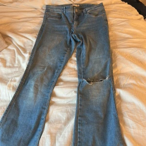 Blå bootcut jeans med hål i - Säljer ett par klassiska blå jeans med bootcut-modell och snygg slitning över ena knät. 