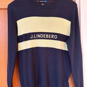 Svart tröja med gul detalj från J.Lindeberg - Snygg svart tröja från J.Lindeberg med breda gula ränder och logga framtill. Tröjan har rund halsringning och långa ärmar. Perfekt för dig som gillar stilrena plagg med en sportig touch. Helt oanvänd, som ny. Nypris 1500 kr. Pris kan diskuteras 