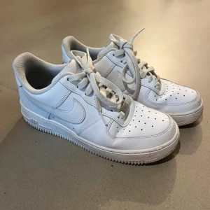 Nike Air Force 1 vita sneakers - Klassiska Nike Air Force 1 sneakers i helvitt skinn med perforerad tå, rund tå och platt sula.