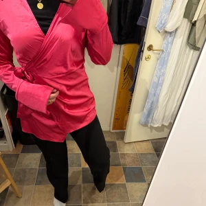 Rosa omlottopp  - Säljer en snygg rosa omlottopp från SHEIN i storlek L. Toppen har långa ärmar, knyt i sidan och en glansig finish som ger en lyxig känsla. Perfekt att ha till både festligare och vardagligare tillfällen! Endast använd en gång vilket innebär att den är i perfekt skick. 