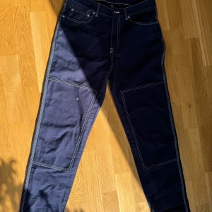 Mörkblå jeansbyxor från Vailent - Säljer ett par mörkblå jeansbyxor från Vailent med kontrasterande vita sömmar och stora fyrkantiga detaljer på benen. Klassisk femficksmodell med raka ben och hög midja. Materialet är kraftigt och passar perfekt till en streetinspirerad look.