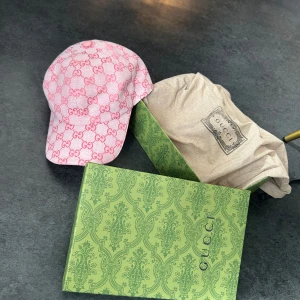 Rosa Gucci keps  - Exklusiv keps från Gucci i ljusrosa bomull med ikoniskt GG-mönster i mörkare rosa. Justerbar rem baktill i rosa läder och klassisk böjd skärm. Kommer med originalbox och dustbag. bra keps i knappast använt skick.